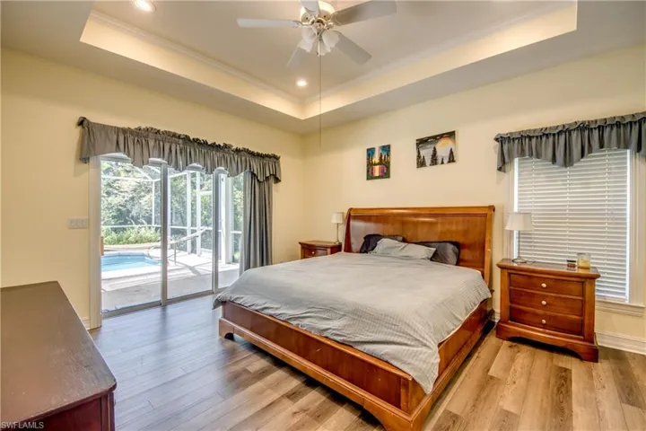Bedroom featuring a tray ceiling, crown molding, access to outside, wood finished floors, and recessed lighting