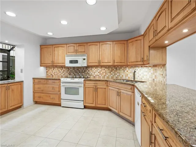 Kitchen with light stone counters, white appliances, recessed lighting, wood finish cabinets, and backsplash