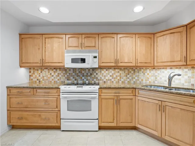 Kitchen with light stone counters, light wood finish cabinetry, tasteful backsplash, and recessed lighting