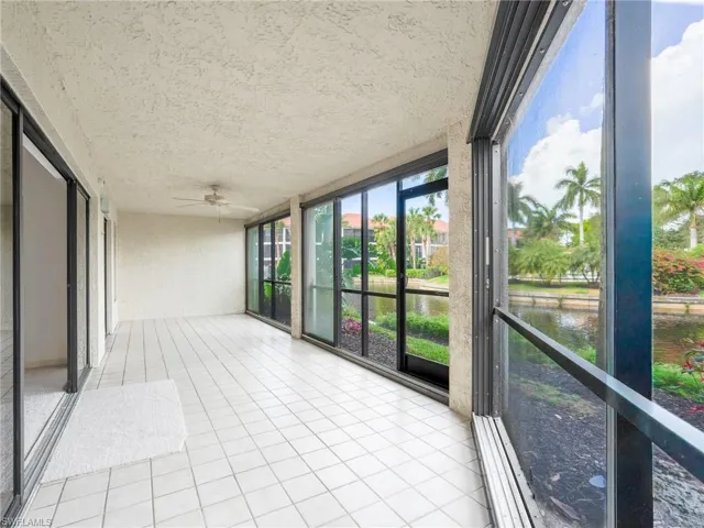 Unfurnished sunroom featuring a water view, ceiling fan, and a balcony