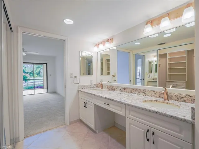 Bathroom with double vanity, light colored carpet, light tile patterned flooring, recessed lighting, and a walk in closet