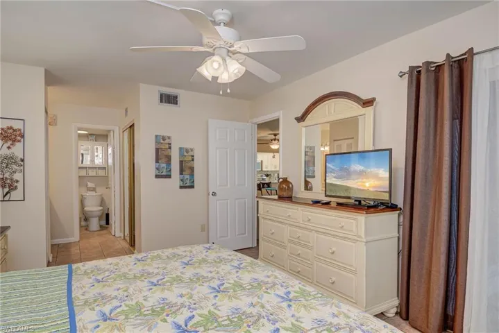 Bedroom with light tile patterned floors, ceiling fan, and ensuite bathroom
