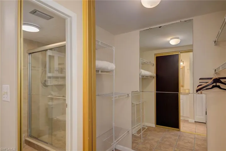 Bathroom with a walk in closet, a shower stall, and light tile patterned floors