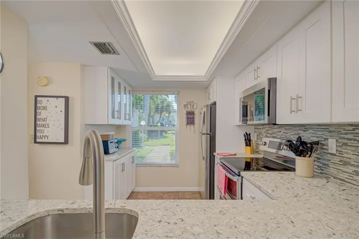 Kitchen with white cabinetry, stainless steel appliances, light stone counters, a tray ceiling, and decorative backsplash