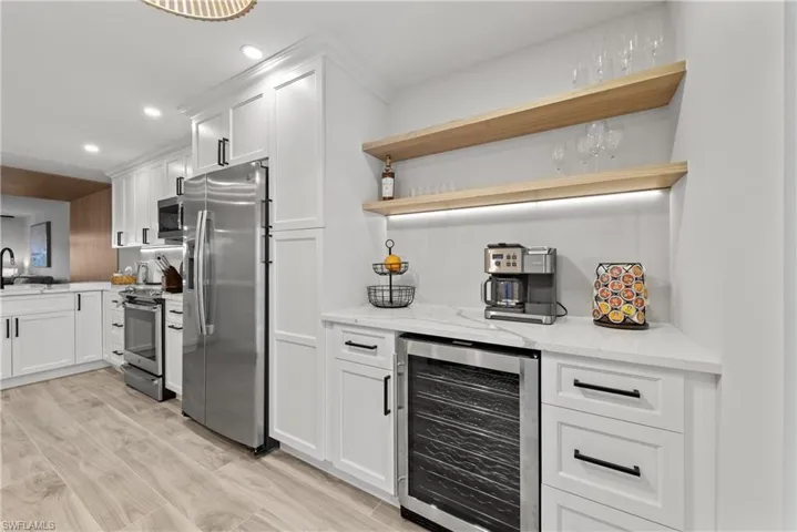 Indoor dry bar featuring open shelves, wine cooler, white cabinetry, appliances with stainless steel finishes, and light stone counters