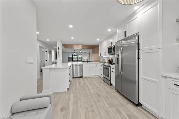 Kitchen with stainless steel appliances, white cabinets, recessed lighting, light wood finished floors, and a peninsula