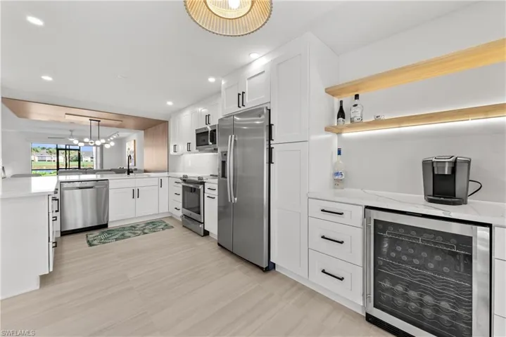 Kitchen with wine cooler, white cabinetry, open shelves, appliances with stainless steel finishes, and light stone counters