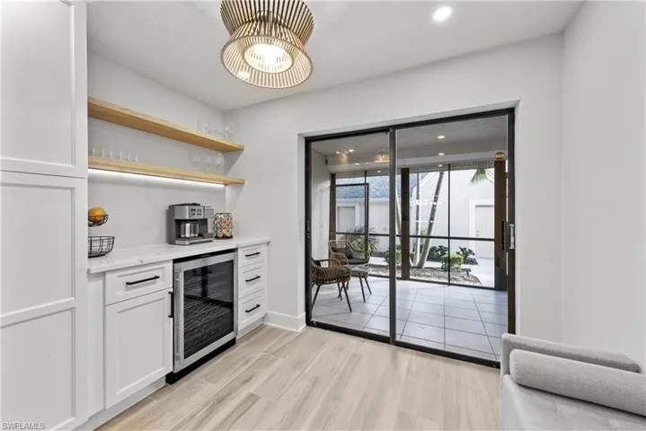 Indoor dry bar with open shelves, wine cooler, white cabinets, light stone counters, and light wood-style floors