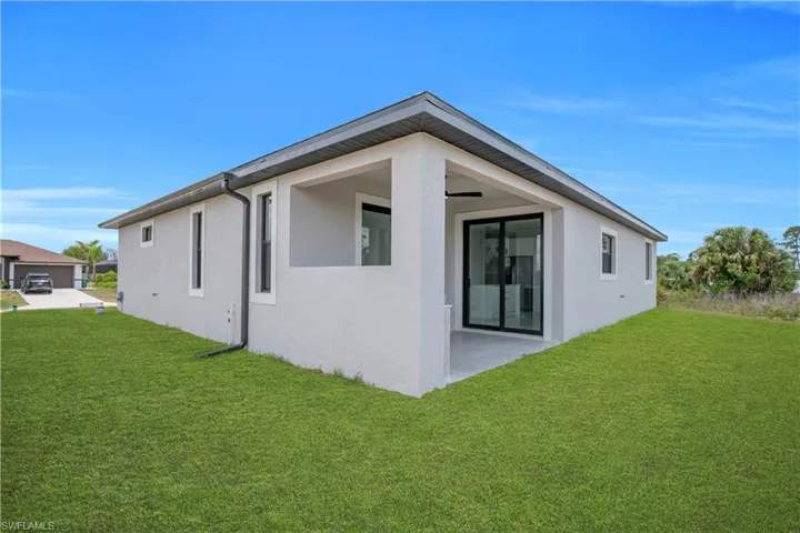 Expansive rear elevation featuring a covered patio, sliding glass doors, and a manicured lawn