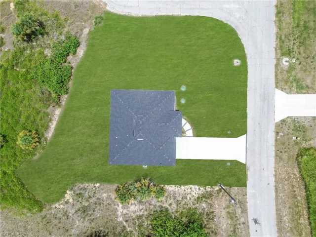 Newly constructed residence featuring a dark shingle roof and a spacious, manicured lawn