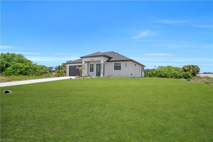 Contemporary single-story residence featuring a two-car garage, a paved driveway, and a well-maintained lawn