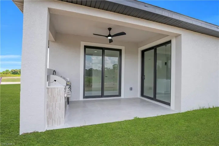 Covered patio featuring an outdoor kitchen with integrated grill, a ceiling fan, and light-toned tile flooring