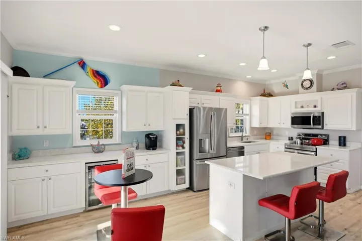 Kitchen with a breakfast bar area, white cabinetry, appliances with stainless steel finishes, light wood-style floors, and ornamental molding