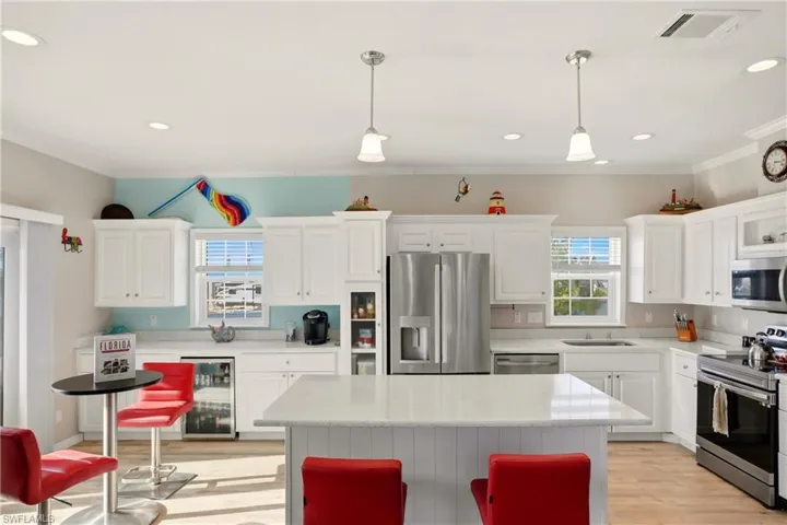 Kitchen with appliances with stainless steel finishes, wine cooler, white cabinets, decorative light fixtures, and crown molding