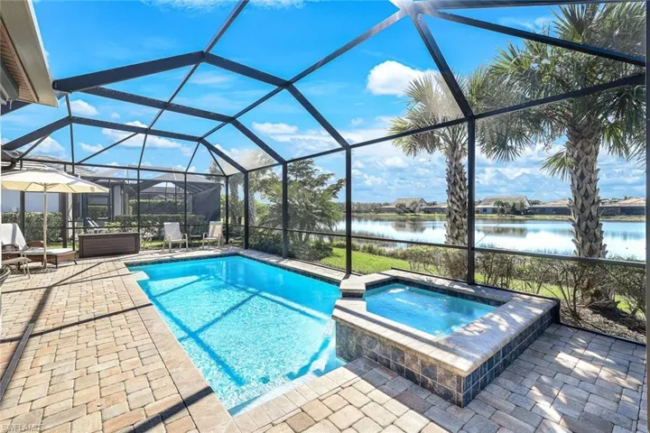 View of swimming pool featuring glass enclosure, an in ground hot tub, a water view, and a patio