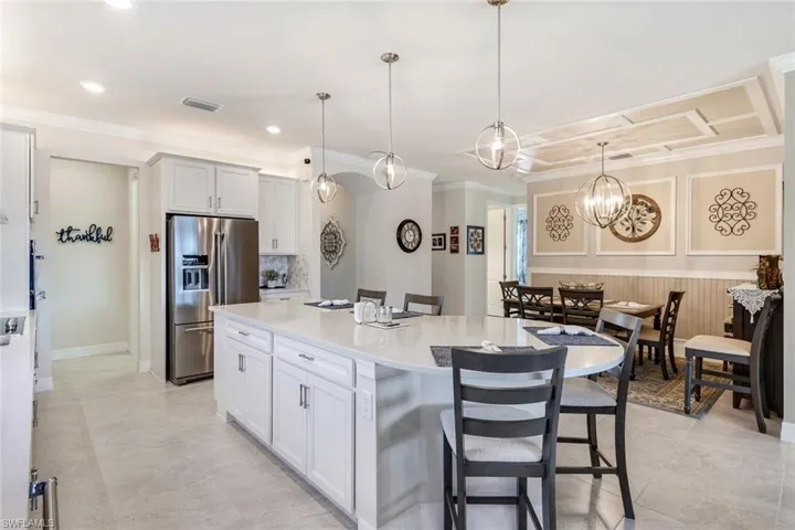 Kitchen featuring a kitchen bar, stainless steel refrigerator with ice dispenser, decorative light fixtures, white cabinets, and a center island