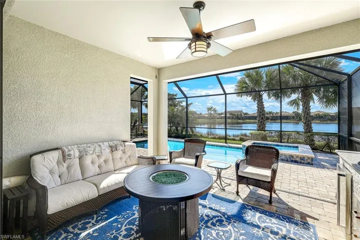 View of patio featuring glass enclosure, a swimming pool with hot tub, a water view, and an outdoor living space with a fire pit