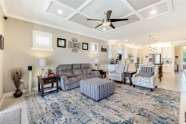 Living room with light tile patterned floors, crown molding, ceiling fan, and coffered ceiling
