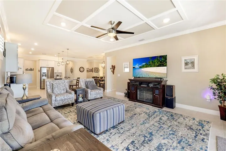 Living room with ceiling fan, light tile patterned floors, ornamental molding, and coffered ceiling