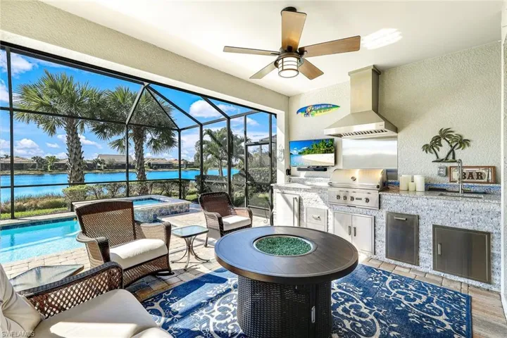 View of patio featuring glass enclosure, a water view, ceiling fan, a grill, and area for grilling