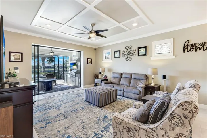 Tiled living room with ceiling fan, crown molding, and coffered ceiling
