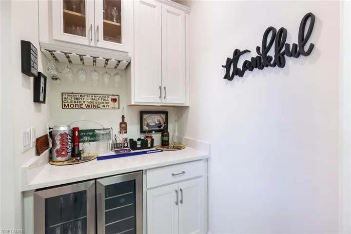 Bar featuring wine cooler, light stone counters, and white cabinets