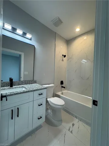 Full bathroom with toilet, tiled shower / bath combo, and vanity