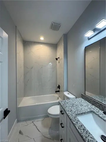 Full guess bathroom with tiled shower / bath combo, vanity, and toilet