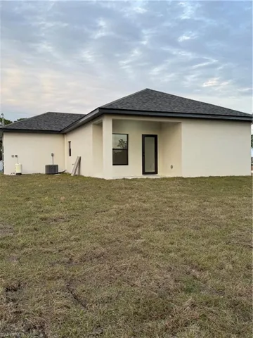 Back of property with central air condition unit and a lawn
