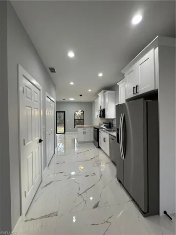 Kitchen with dishwasher, hanging light fixtures, white cabinets, fridge, and stove