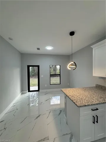 Kitchen with decorative light fixtures, white cabinets, and light stone counters
