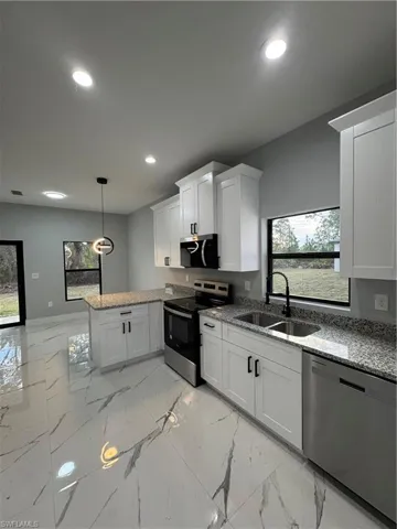 Kitchen featuring decorative light fixtures, dishwashing machine, white cabinetry, stove, and sink