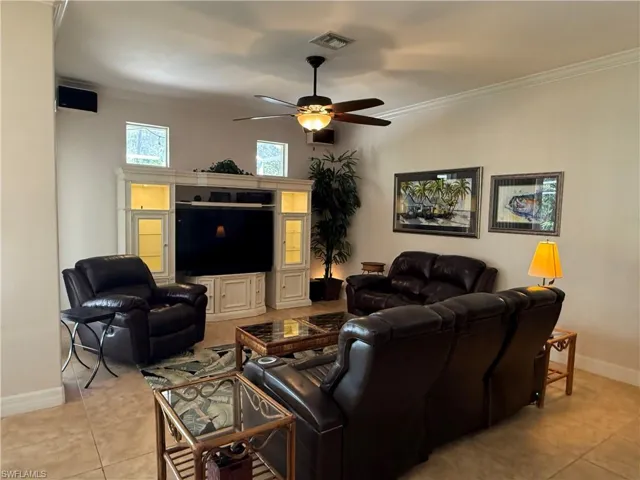 Tiled living room with ornate columns, ceiling fan, and ornamental molding