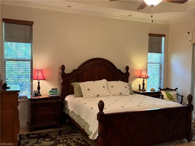 Tiled bedroom with a raised ceiling, ceiling fan, and ornamental molding