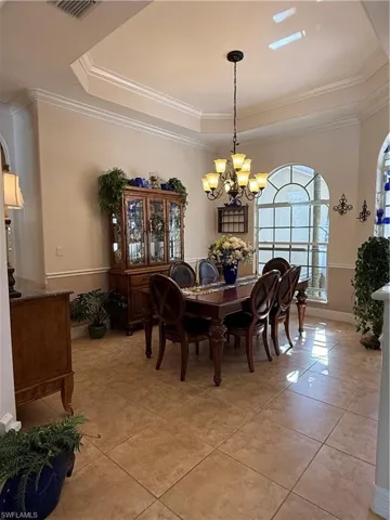 Tiled dining room with ornamental molding, a tray ceiling, and a notable chandelier