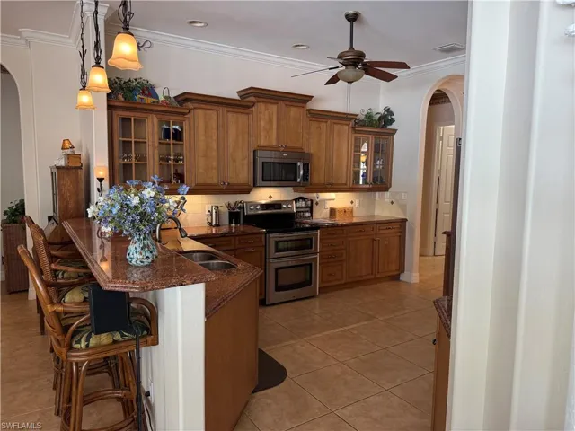 Kitchen featuring a kitchen bar, appliances with stainless steel finishes, tasteful backsplash, dark stone counters, and pendant lighting