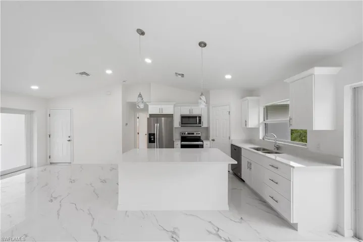 Kitchen with a kitchen island, vaulted ceiling, sink, pendant lighting, and stainless steel appliances