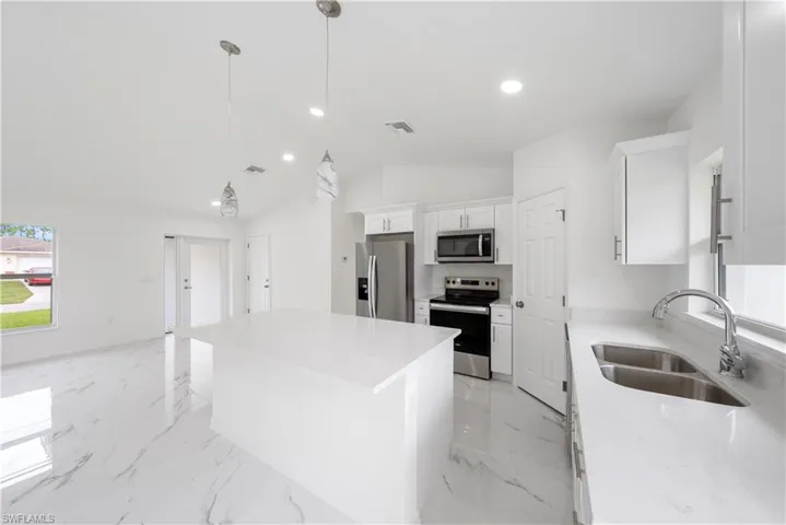 Kitchen featuring sink, a center island, white cabinetry, stainless steel appliances, and lofted ceiling