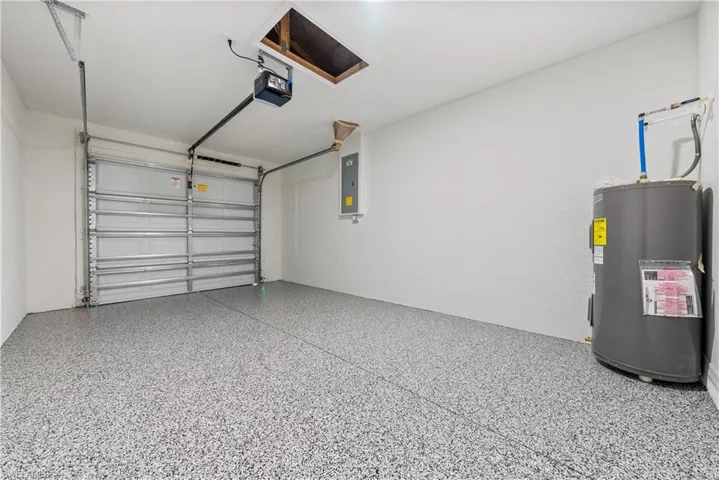 Garage featuring electric panel, electric water heater, and a garage door opener