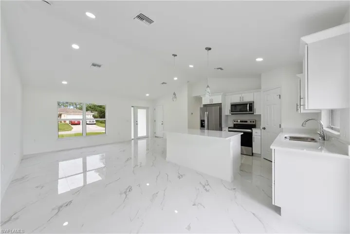 Kitchen with lofted ceiling, a kitchen island, sink, white cabinetry, and appliances with stainless steel finishes