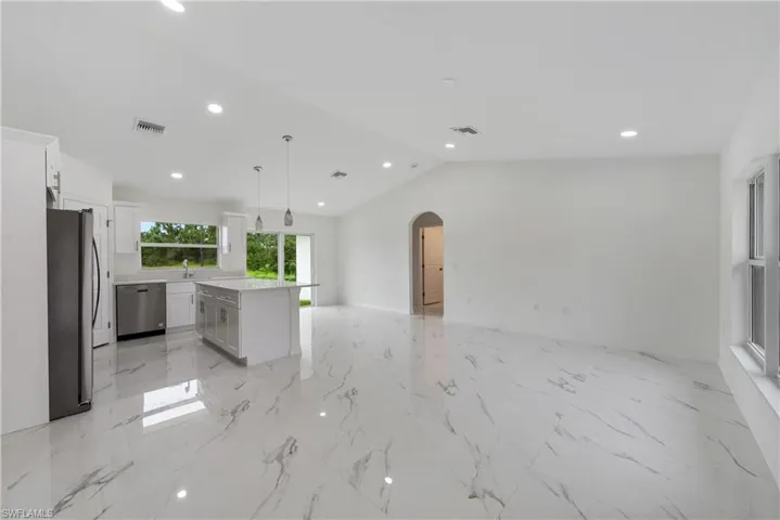 Kitchen with appliances with stainless steel finishes, a center island, hanging light fixtures, white cabinetry, and vaulted ceiling