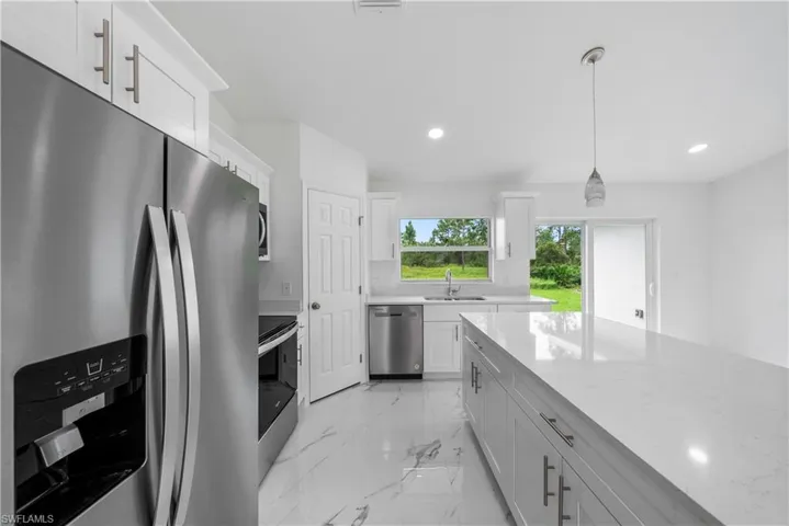 Kitchen with hanging light fixtures, stainless steel appliances, sink, white cabinetry, and light stone counters