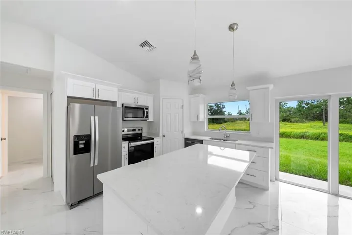 Kitchen with appliances with stainless steel finishes, a center island, hanging light fixtures, vaulted ceiling, and white cabinets