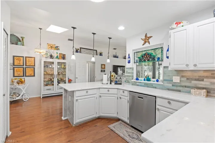 Kitchen featuring stainless steel dishwasher, a peninsula, decorative backsplash, wood finished floors, and white cabinets
