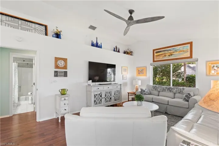 Living area featuring dark wood-style flooring, a ceiling fan, and vaulted ceiling