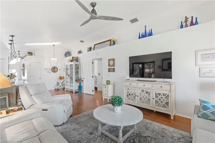 Living room featuring wood finished floors, vaulted ceiling, ceiling fan, and a chandelier