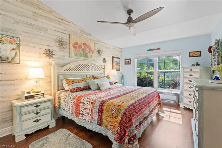 Bedroom featuring wooden walls, vaulted ceiling, dark wood finished floors, and ceiling fan