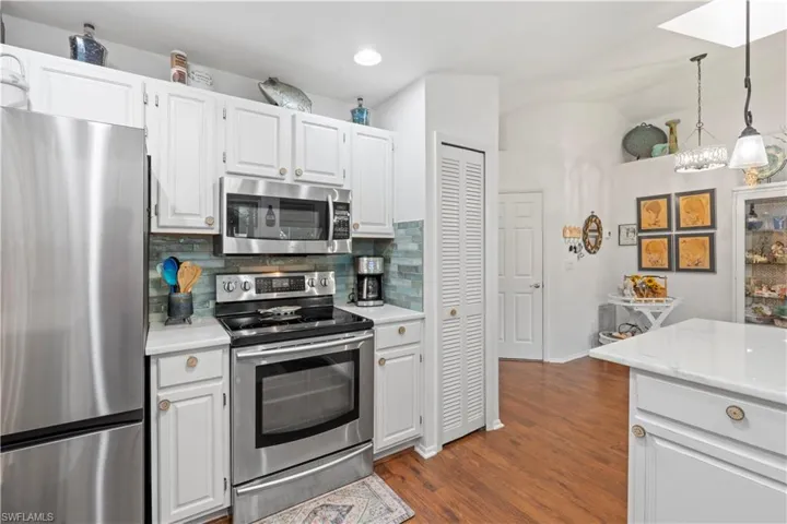 Kitchen featuring stainless steel appliances, light countertops, tasteful backsplash, dark wood finished floors, and hanging light fixtures