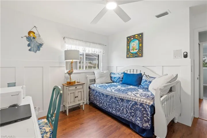 Bedroom featuring a decorative wall, a wainscoted wall, wood finished floors, and a ceiling fan