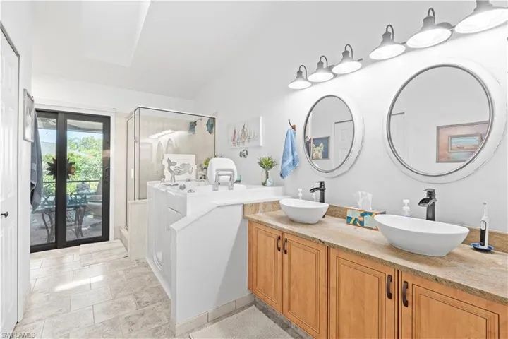 Bathroom featuring a stall shower, double vanity, and lofted ceiling